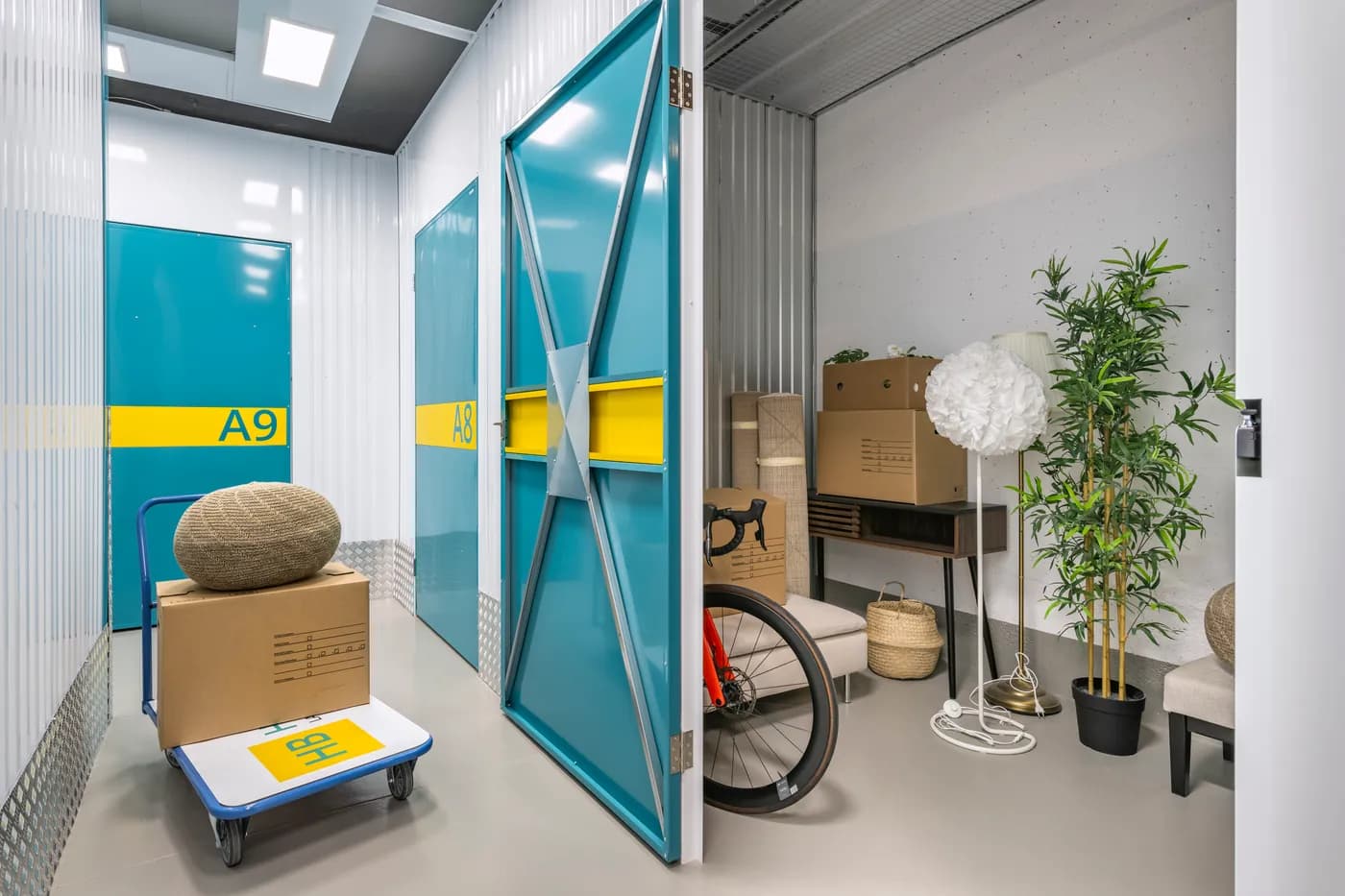 Offene Lagerbox bei HubliBox in Spreitenbach mit eingelagerten Möbeln, Kartons und einem Fahrrad, davor ein Rollwagen